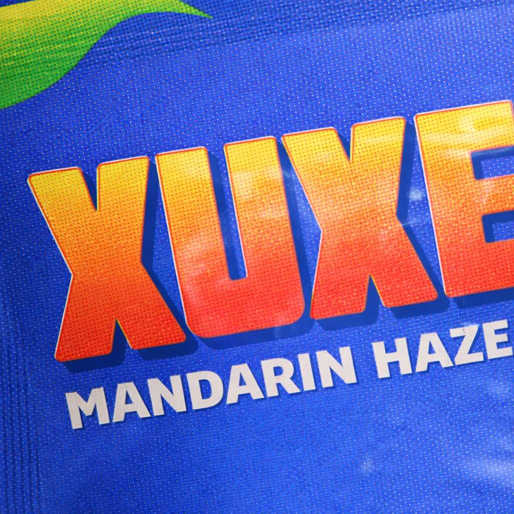 Detalle del envase Xuxes con el texto Mandarin Haze sobre fondo azul y textura del material visible